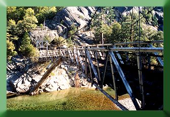 Upriver side; flood damaged bridge is deflected and bent, with log jammed into the truss.